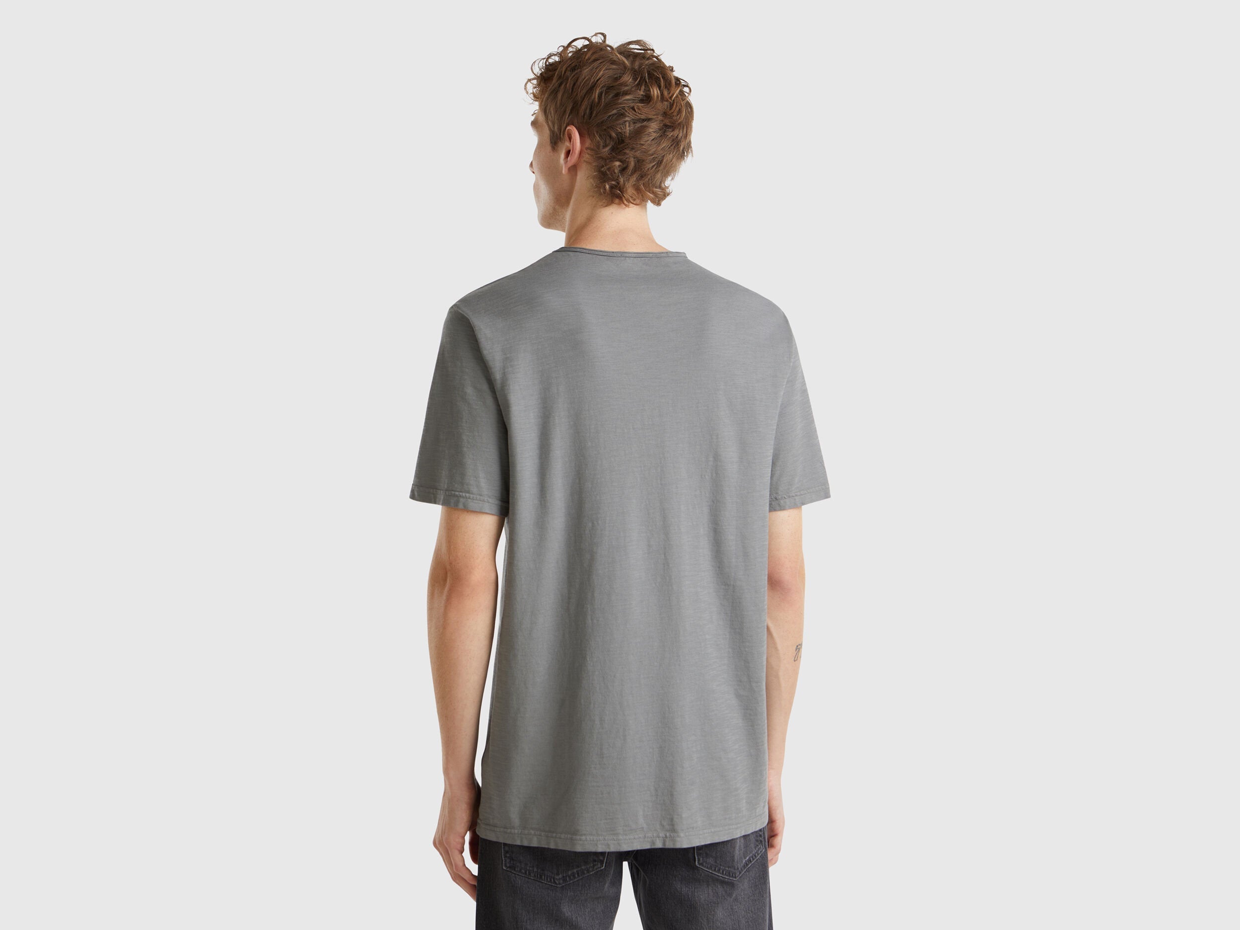 Male model wearing a grey Benetton V-neck T-shirt made of 100% cotton, posing from the back.