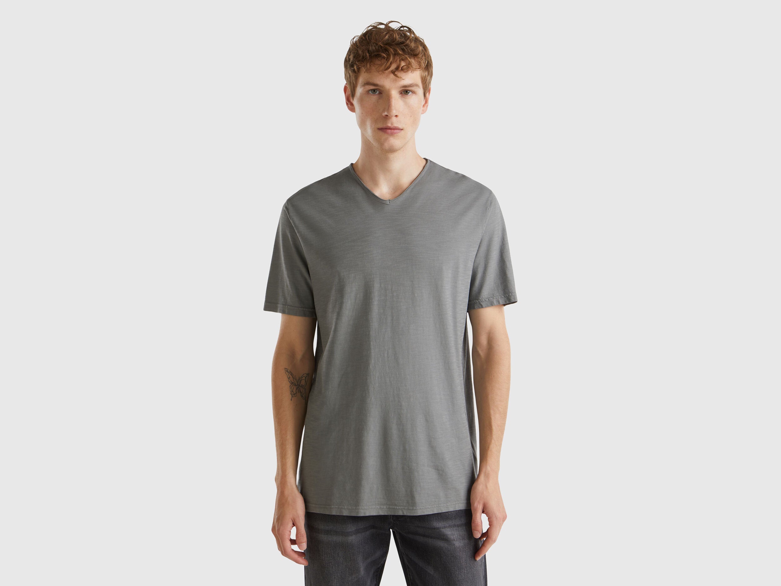 Male model wearing a grey Benetton V-neck T-shirt made of 100% cotton, posing from the front.
