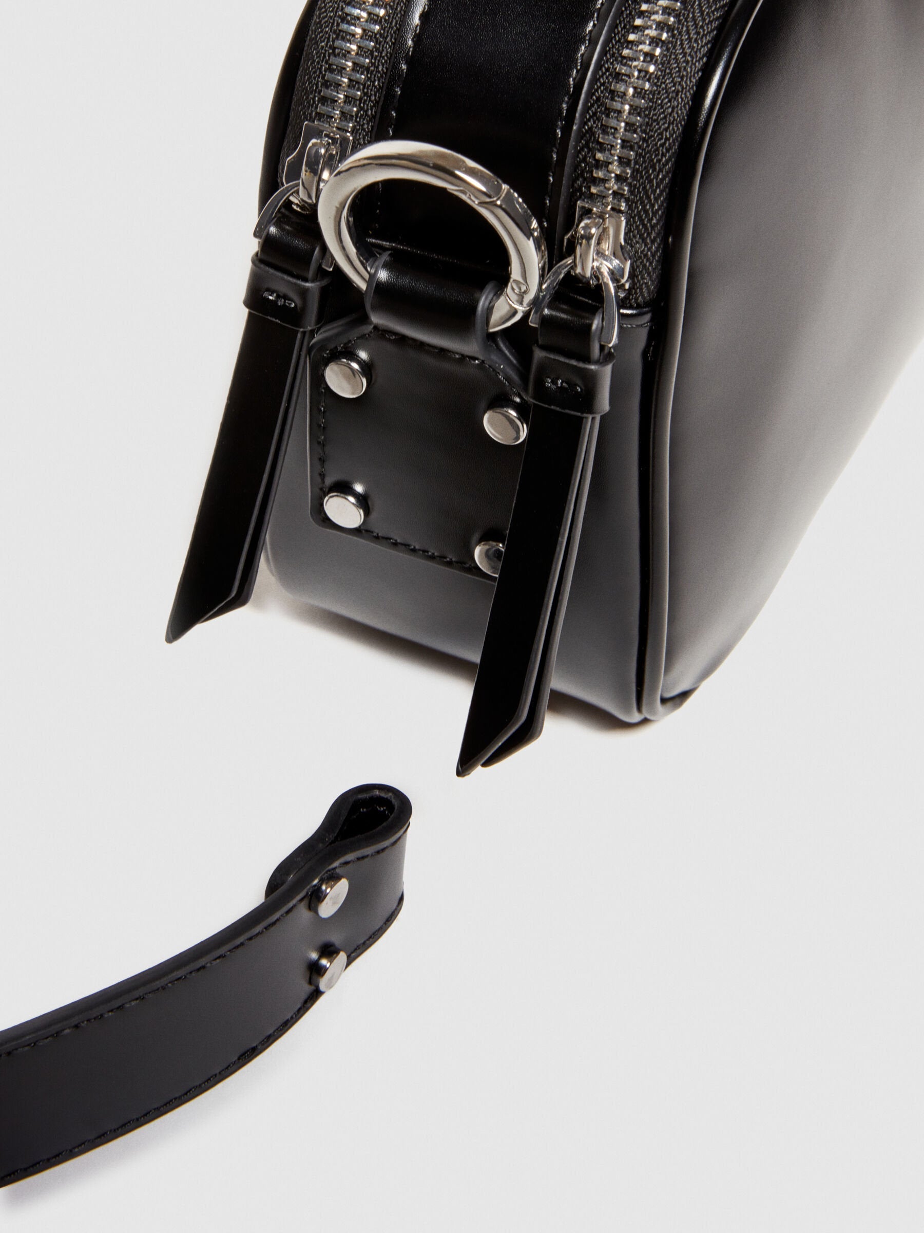 Close-up detail of the black leather camera bag or messenger bag, highlighting the top zipper closure and metal hardware.