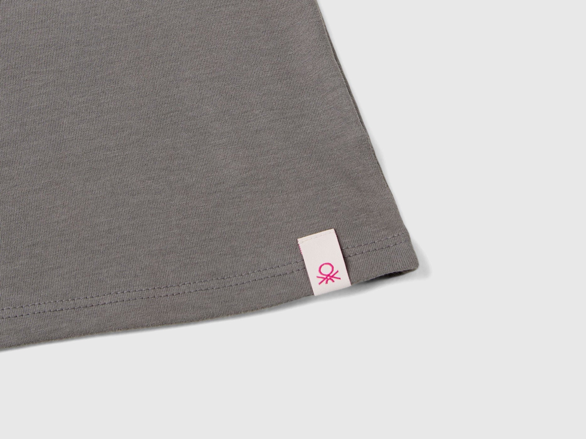 Close-up of the grey long-sleeve t-shirt hem, showing a small Benetton tag.