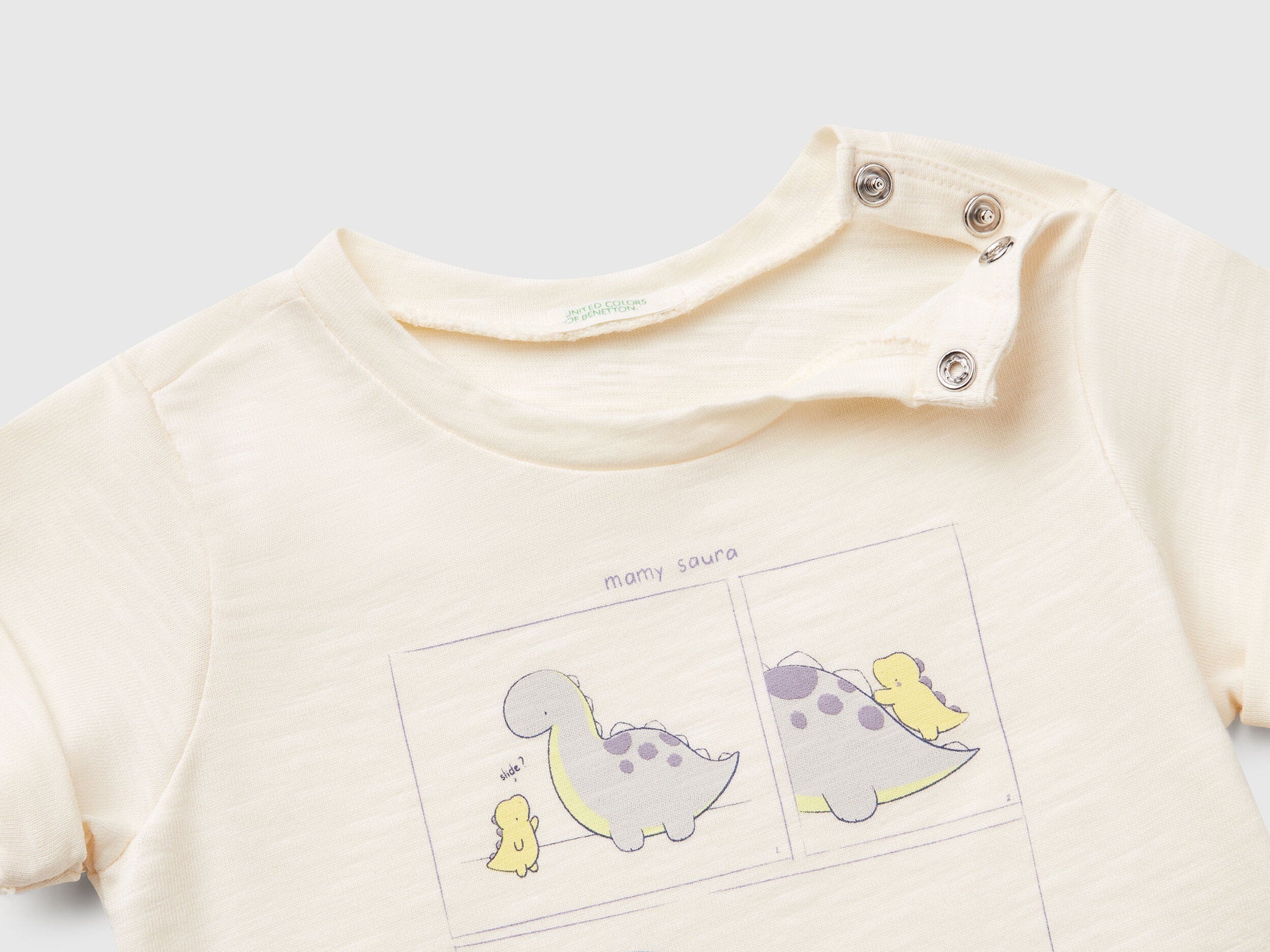 Close-up of the neckline and shoulder snaps on an off-white T-shirt for kids in Kuwait, with a subtle dinosaur graphic, designed for easy dressing.