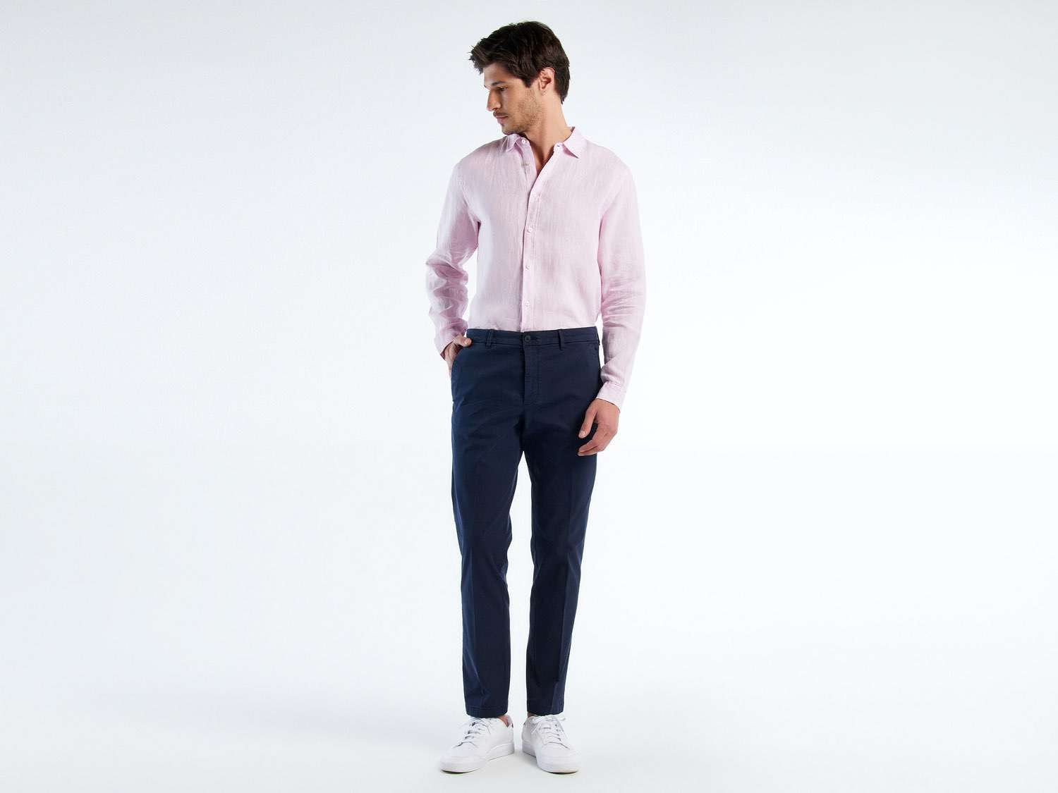 Full shot of a man wearing navy trousers and a light pink shirt.