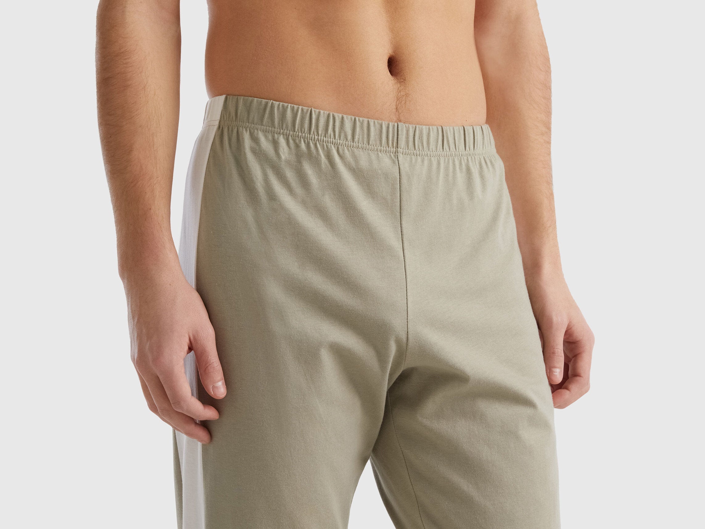 Close-up of beige pyjama bottoms for men, showing the elastic waistband and side stripe.