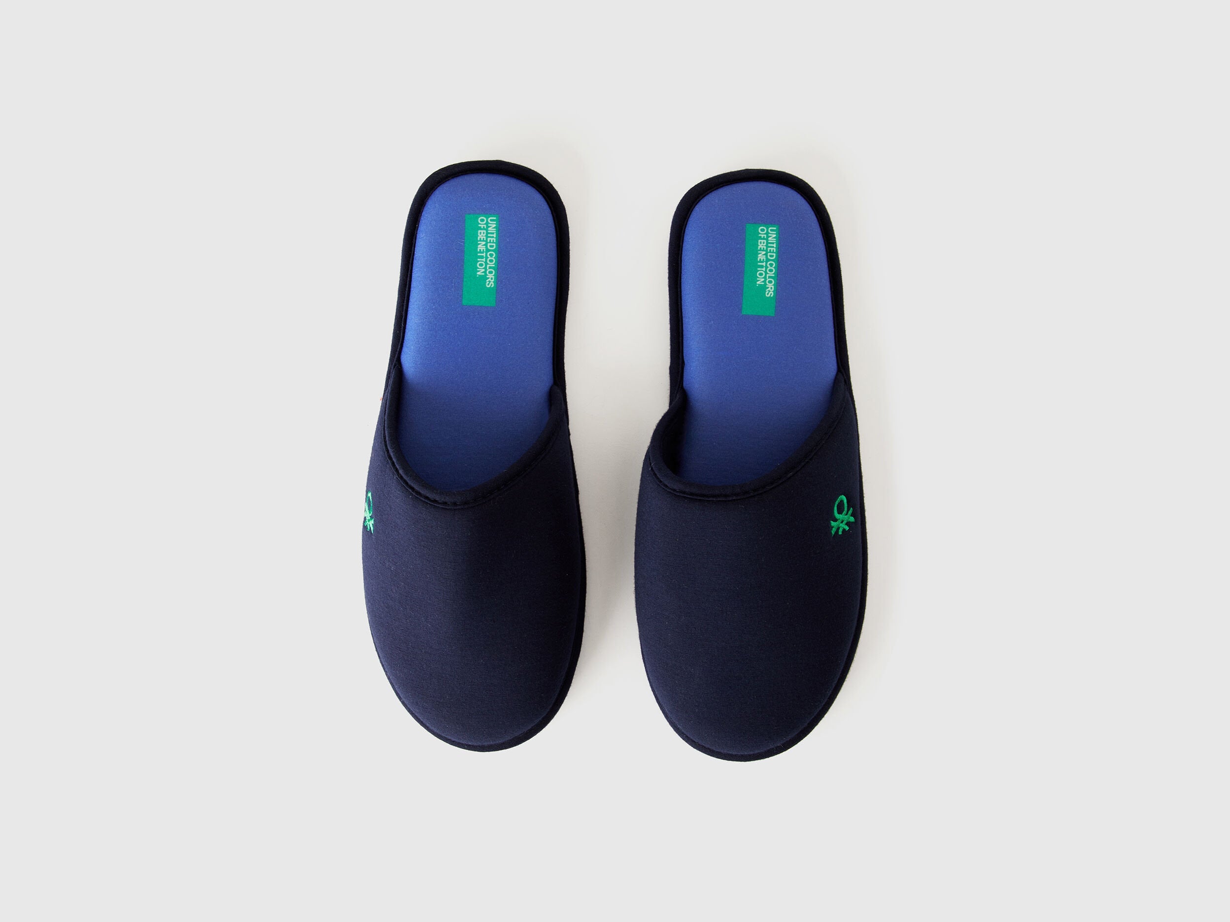 Top view of a pair of navy blue slippers with blue insoles and a green logo.