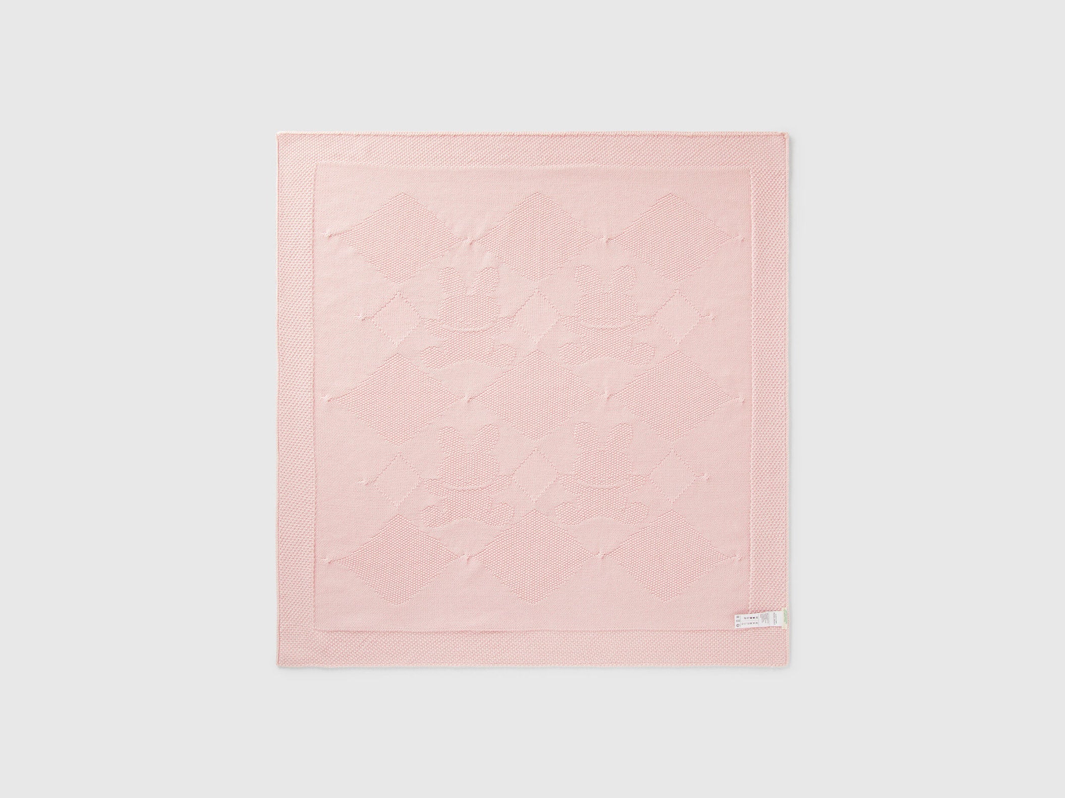 Folded light pink Benetton knit baby blanket, showing textured weave and corner detail.