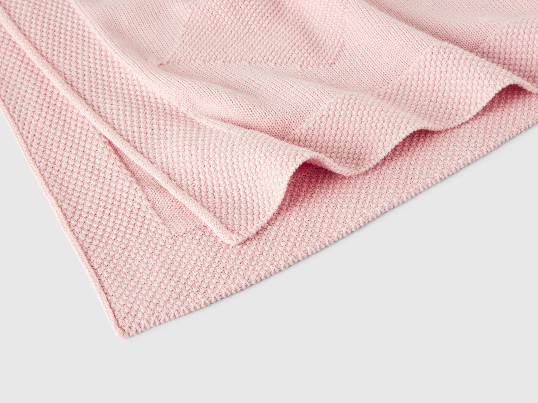 Close-up of a light pink Benetton knit baby blanket, highlighting its soft, ribbed texture.