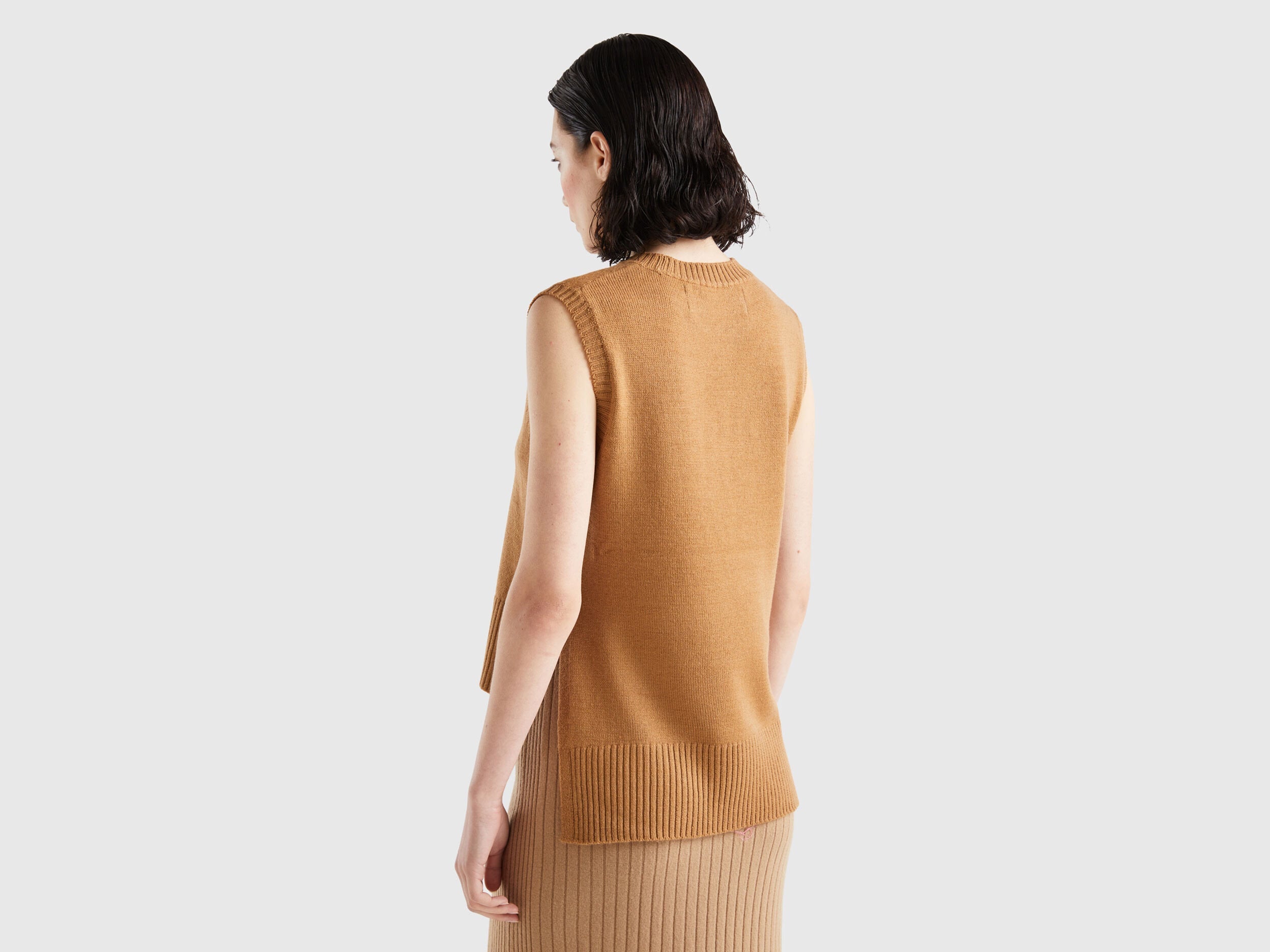 Back view of a woman wearing a light brown knit vest and matching skirt.
