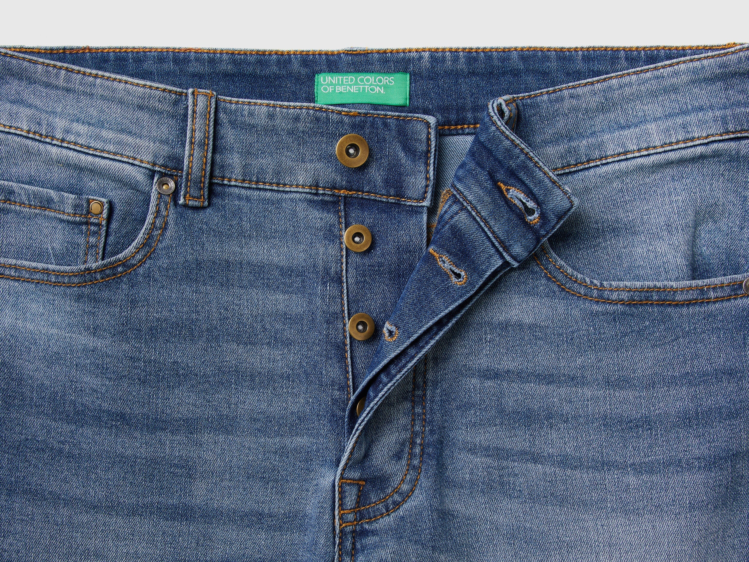 Close-up of the waistband and front button closure on black slim-fit jeans.