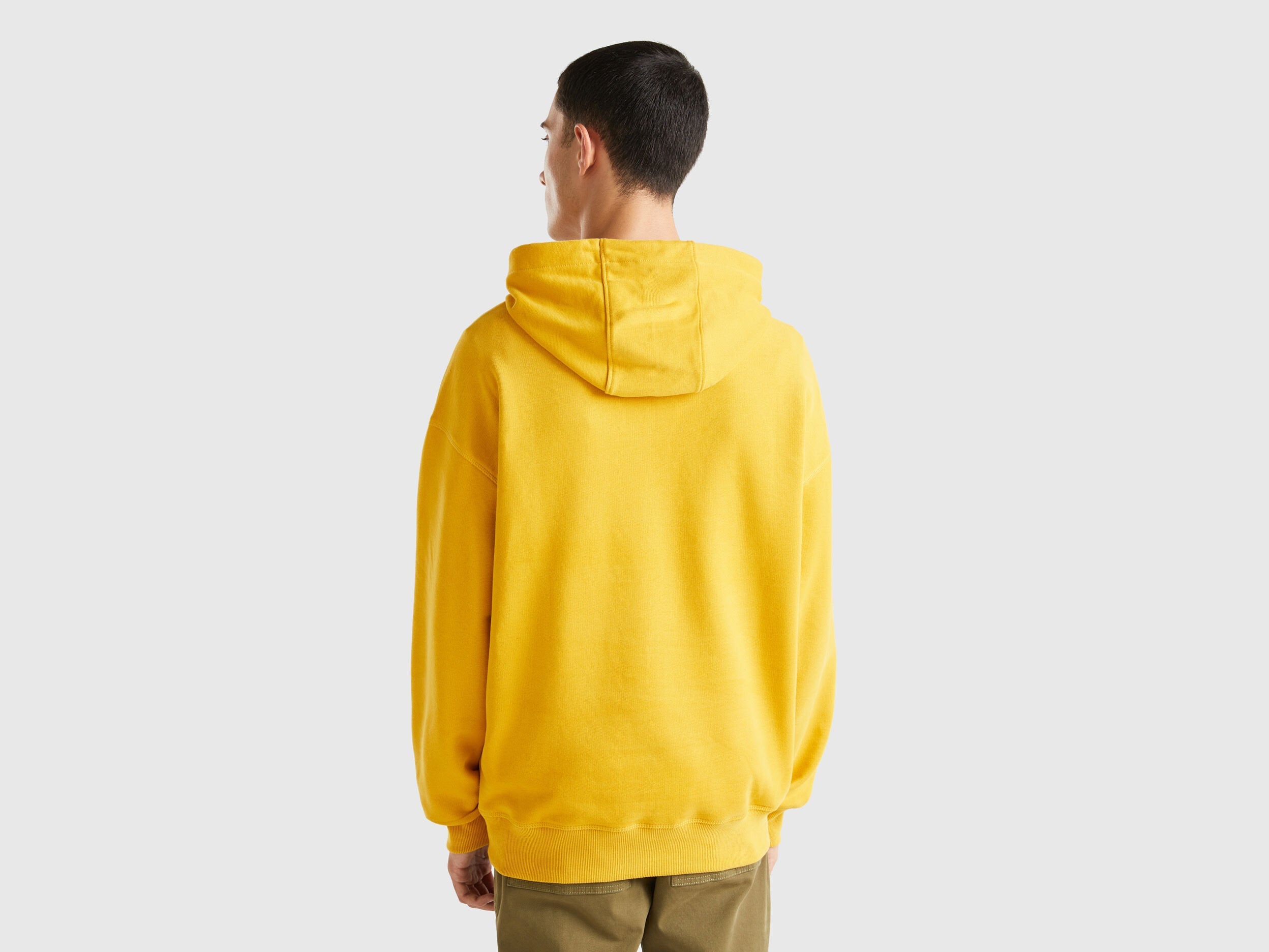 Back view of a man wearing a yellow hoodie with a graphic print.