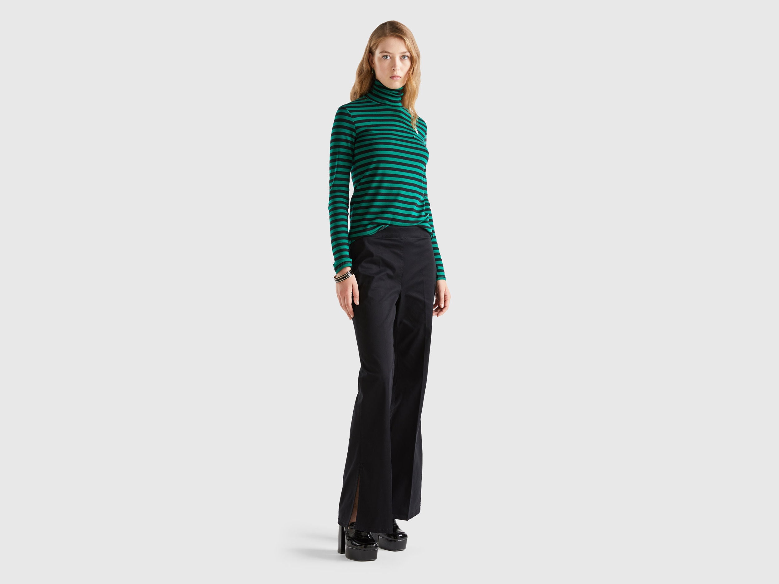Front view of a woman wearing black flared pants and a striped green top.