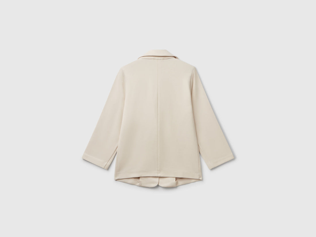 Back view of a light beige elegant long blazer. Features a smooth, tailored fit with subtle pleating.