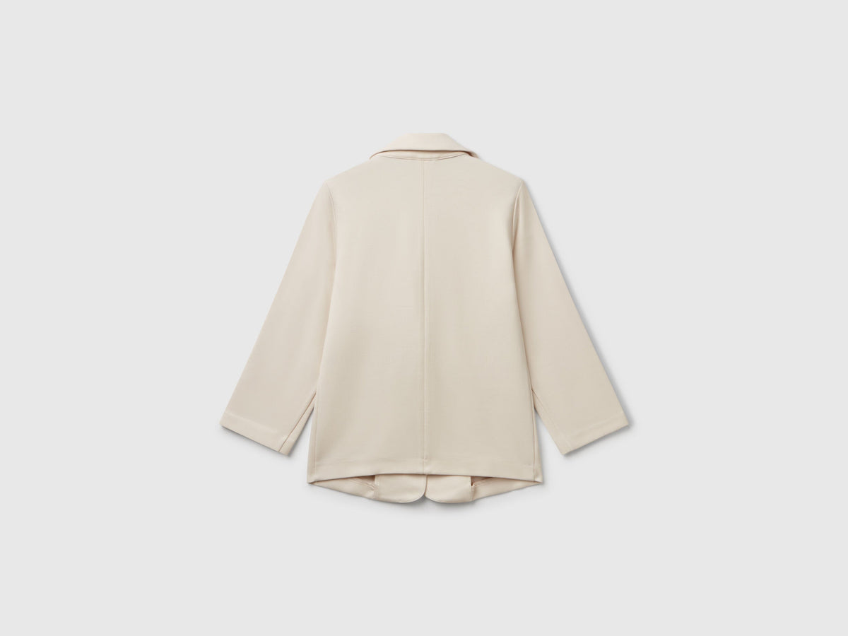 Back view of a light beige elegant long blazer. Features a smooth, tailored fit with subtle pleating.