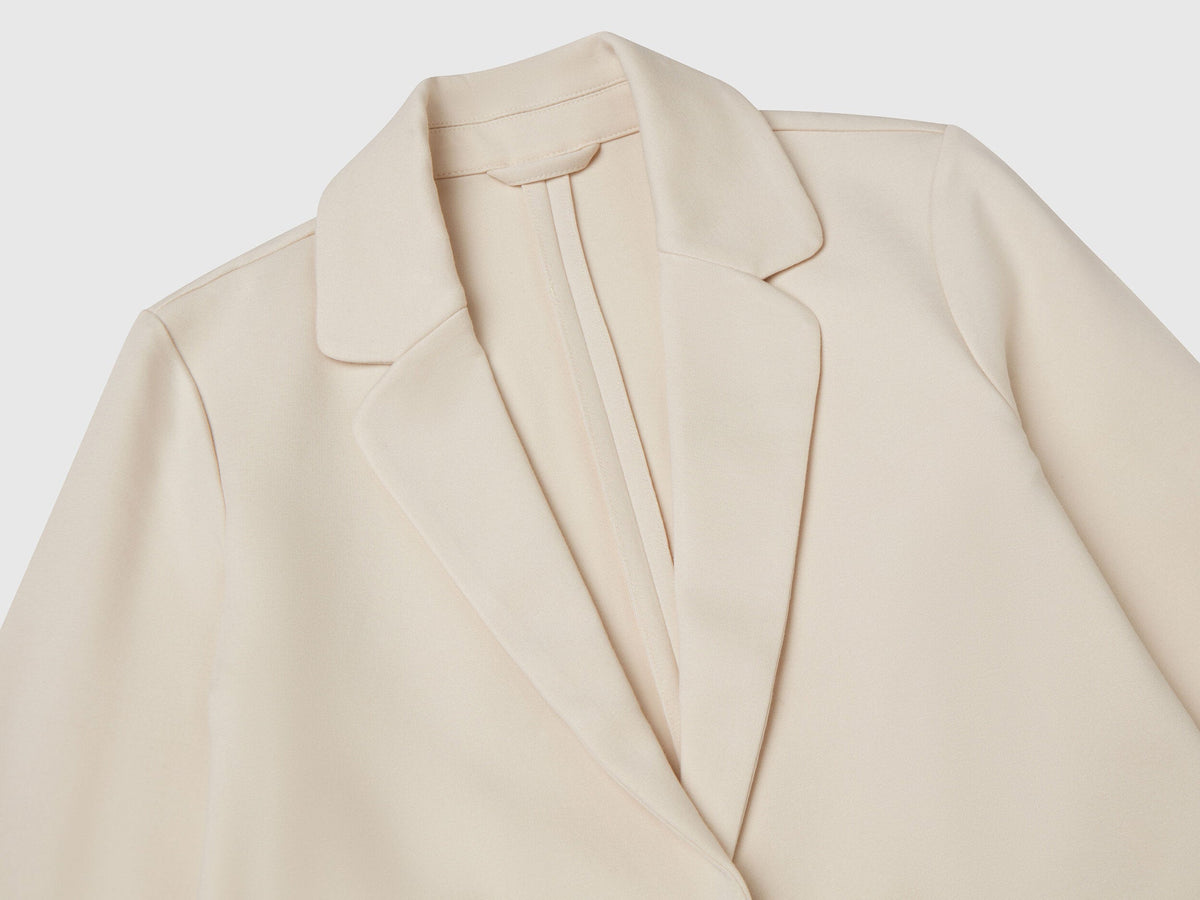 Close-up of a light beige elegant long blazer, showing the lapel, collar, and fabric texture.