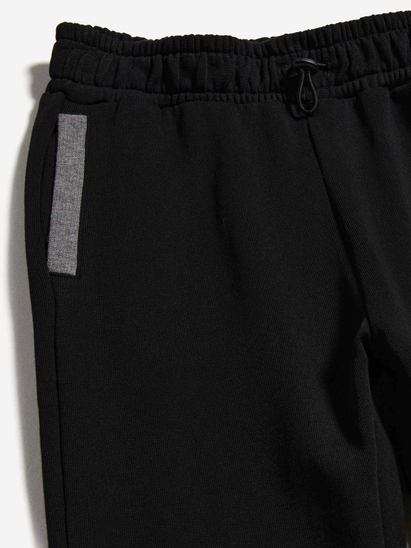 Close-up detail of the black clashing jogger sweatpants, showing the texture of the fabric and the reflective side stripe.