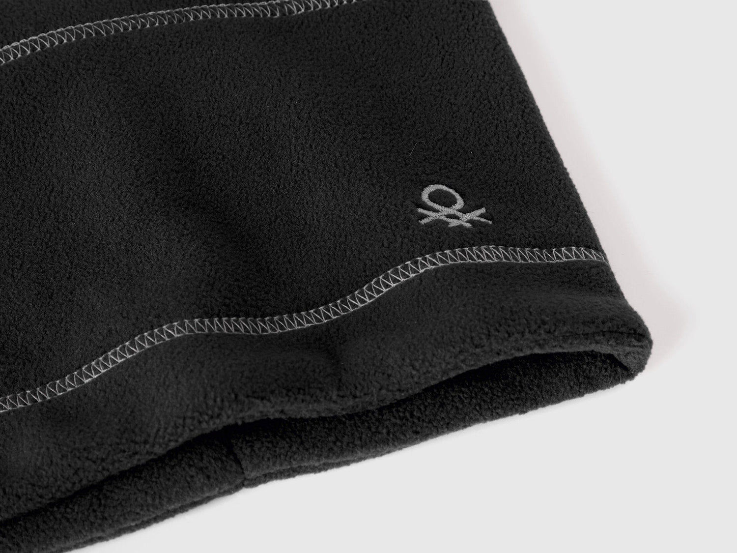 Close-up of black fleece neck warmer with Benetton logo.