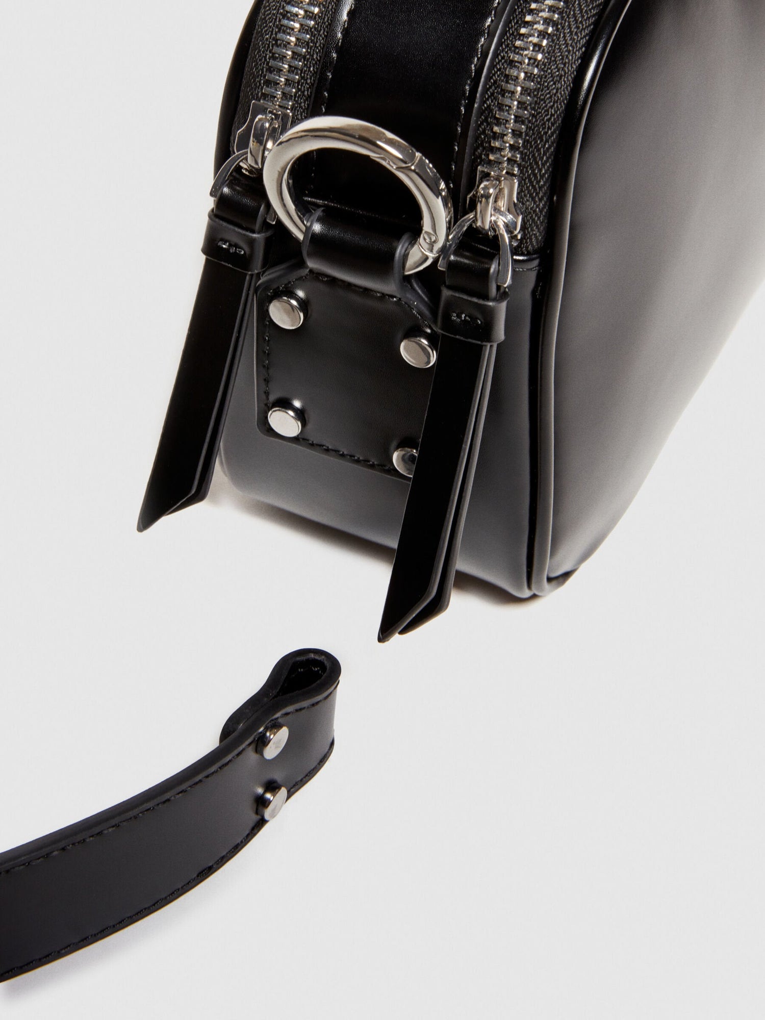 Close-up detail of the black leather camera bag or messenger bag, highlighting the top zipper closure and metal hardware.