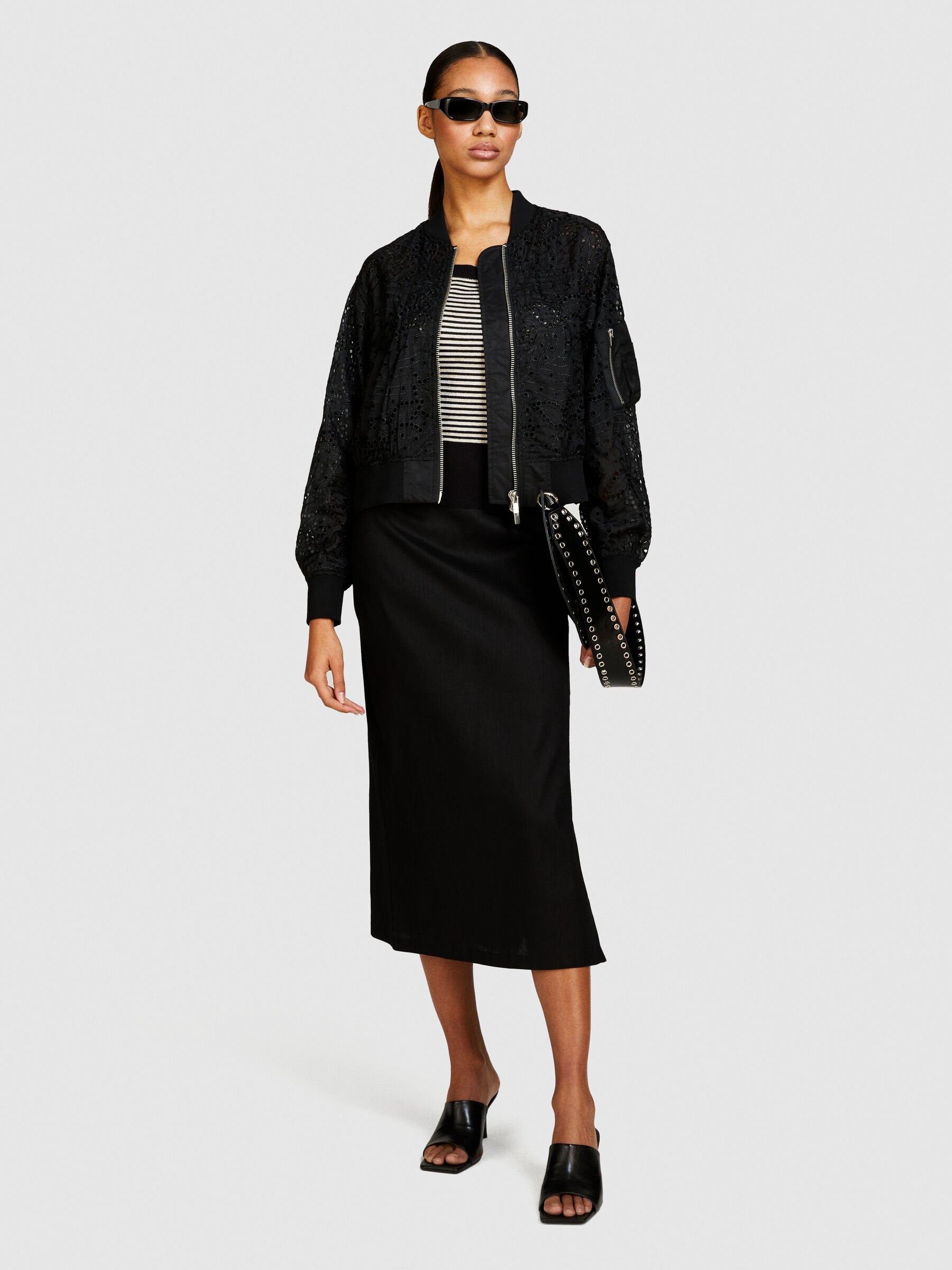 Front view of model wearing a black pencil skirt and bomber jacket with sunglasses.