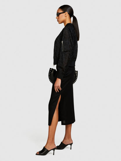Side view of model wearing a black pencil skirt with a high side slit.