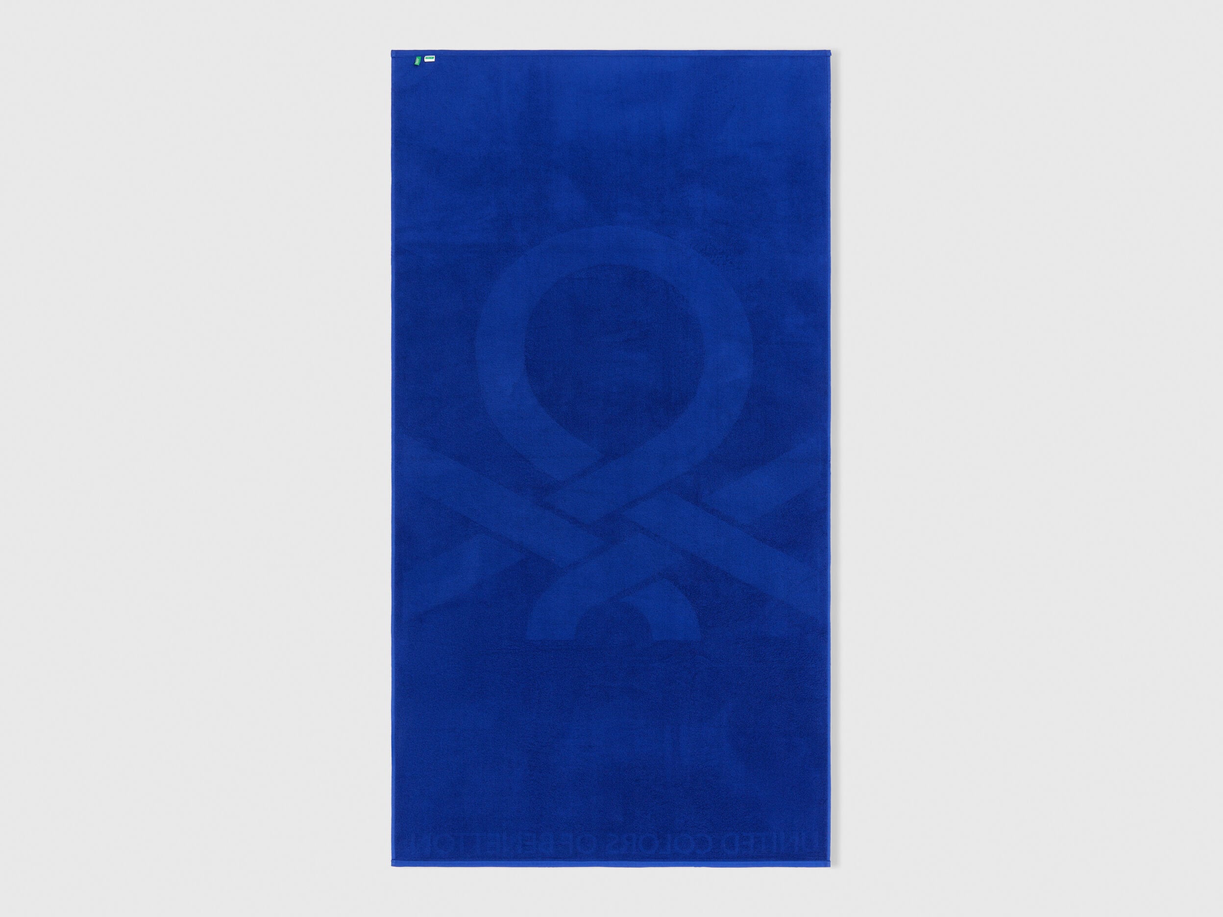 Folded blue Benetton beach towel, showcasing its soft texture and compact size. Travel-friendly.