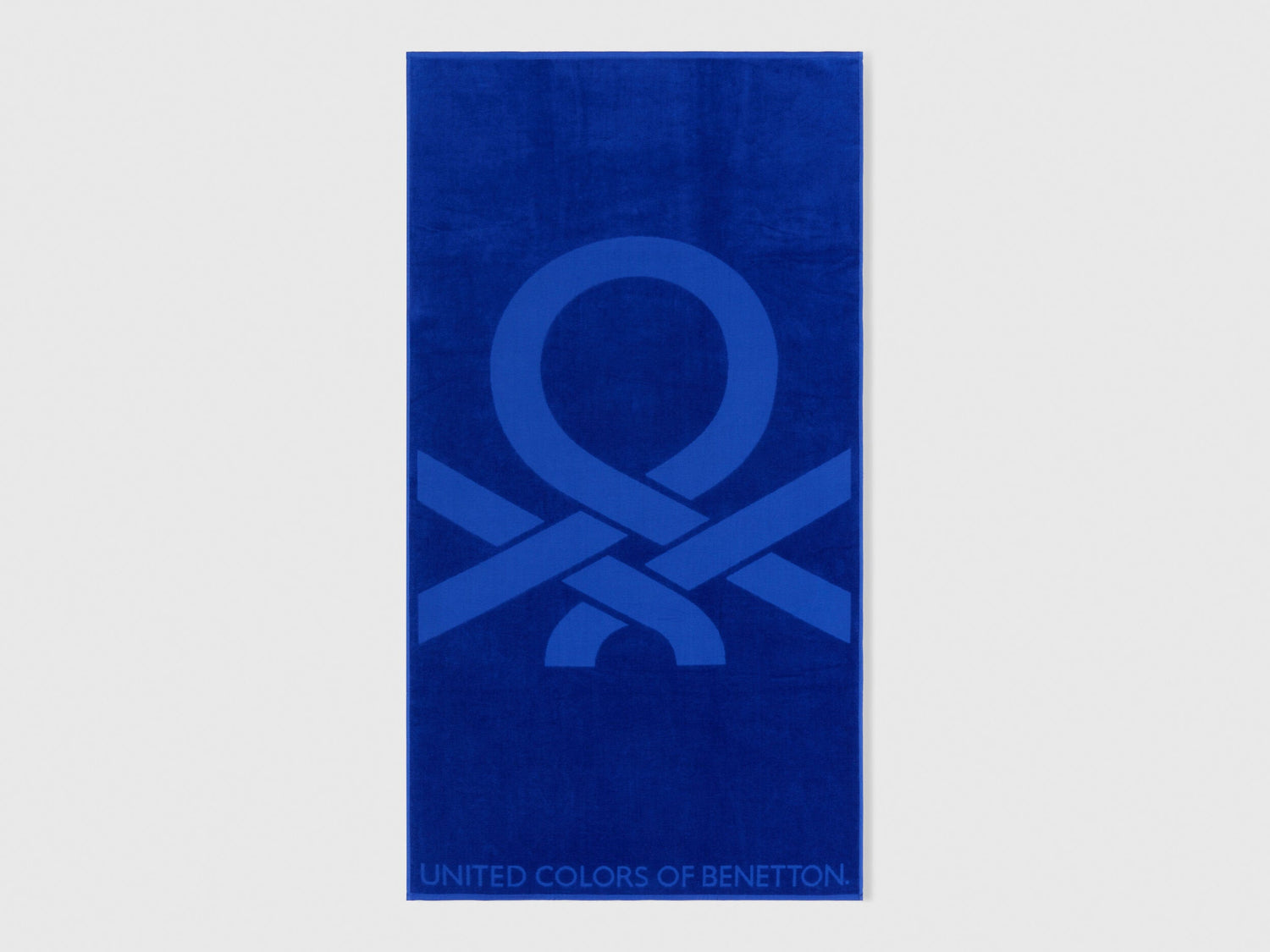Full view of a vibrant blue Benetton beach towel with large brand logo. Soft and absorbent.