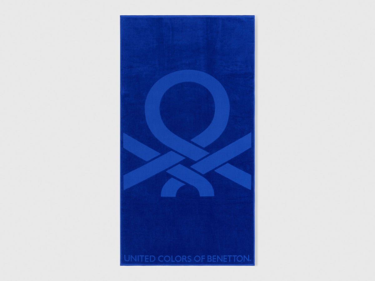 Full view of a vibrant blue Benetton beach towel with large brand logo. Soft and absorbent.