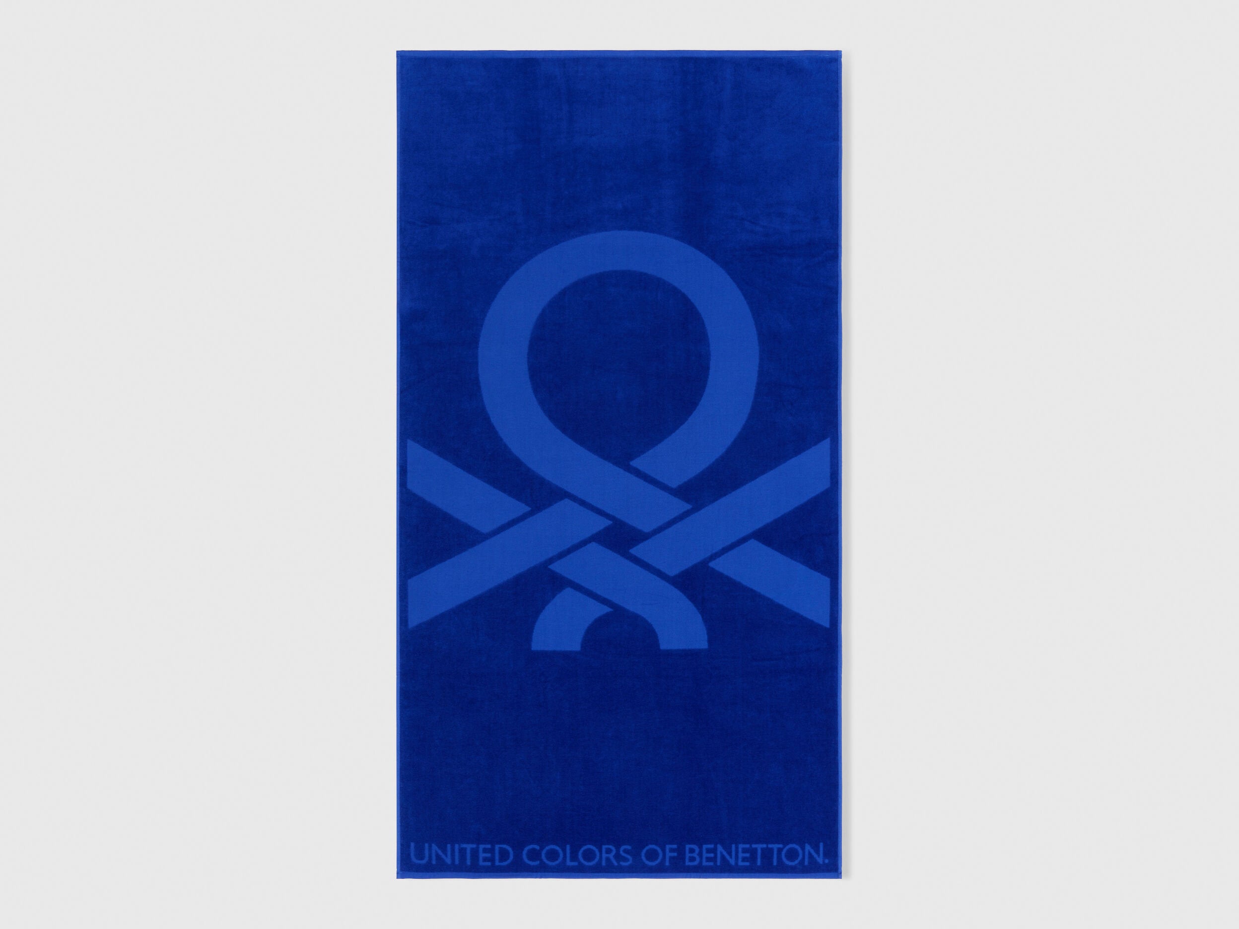 Full view of a vibrant blue Benetton beach towel with large brand logo. Soft and absorbent.