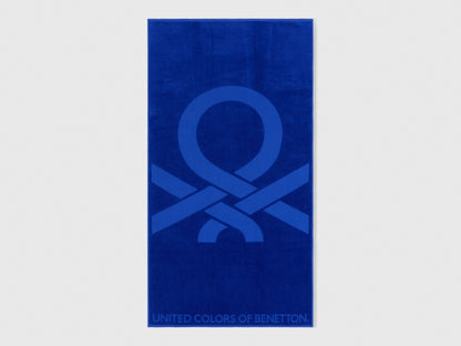 Full view of a vibrant blue Benetton beach towel with large brand logo. Soft and absorbent.