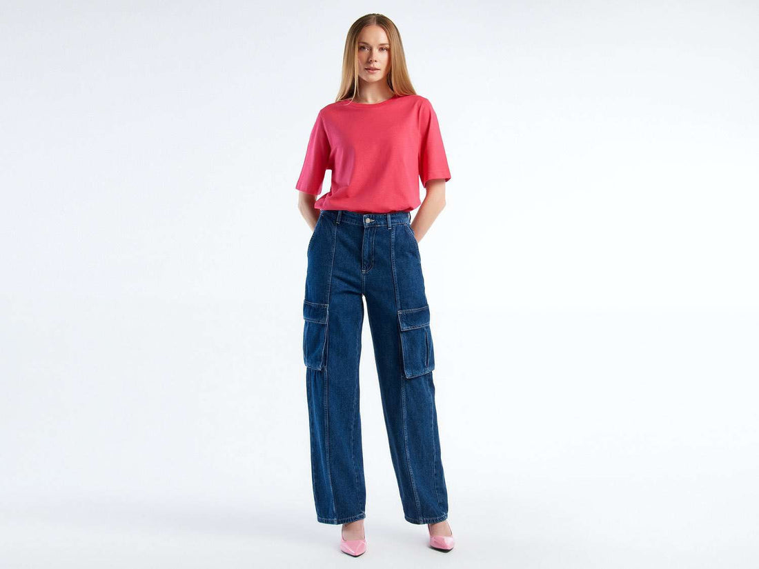 Front view of a woman wearing dark blue cargo trousers with a pink top and heels. Casual style.