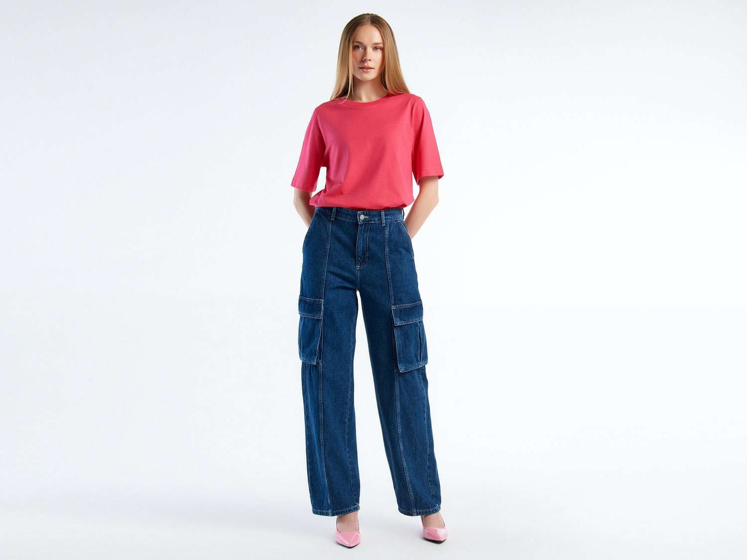 Front view of a woman wearing dark blue cargo trousers with a pink top and heels. Casual style.
