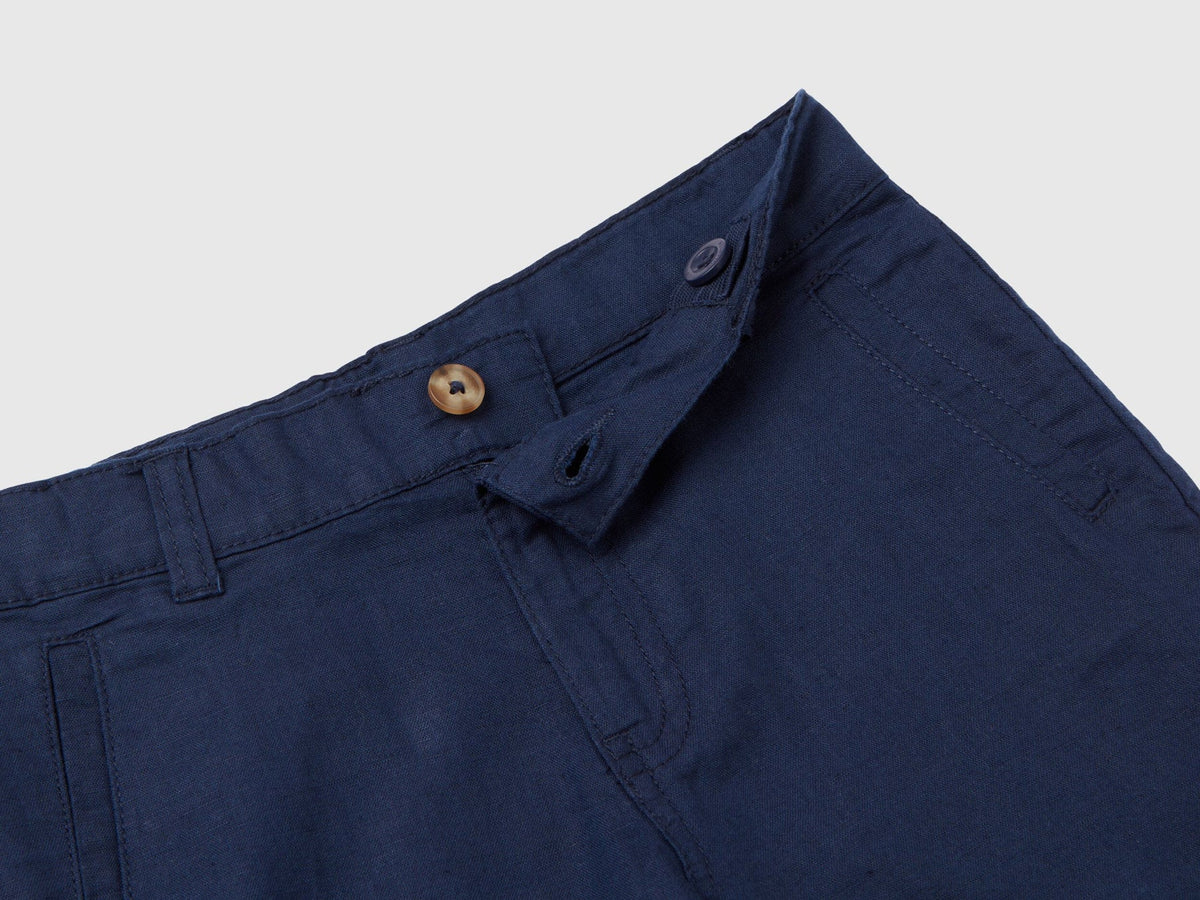 A close-up view of the fly and waist details of dark blue linen blend shorts, showing the button closure and belt loops.