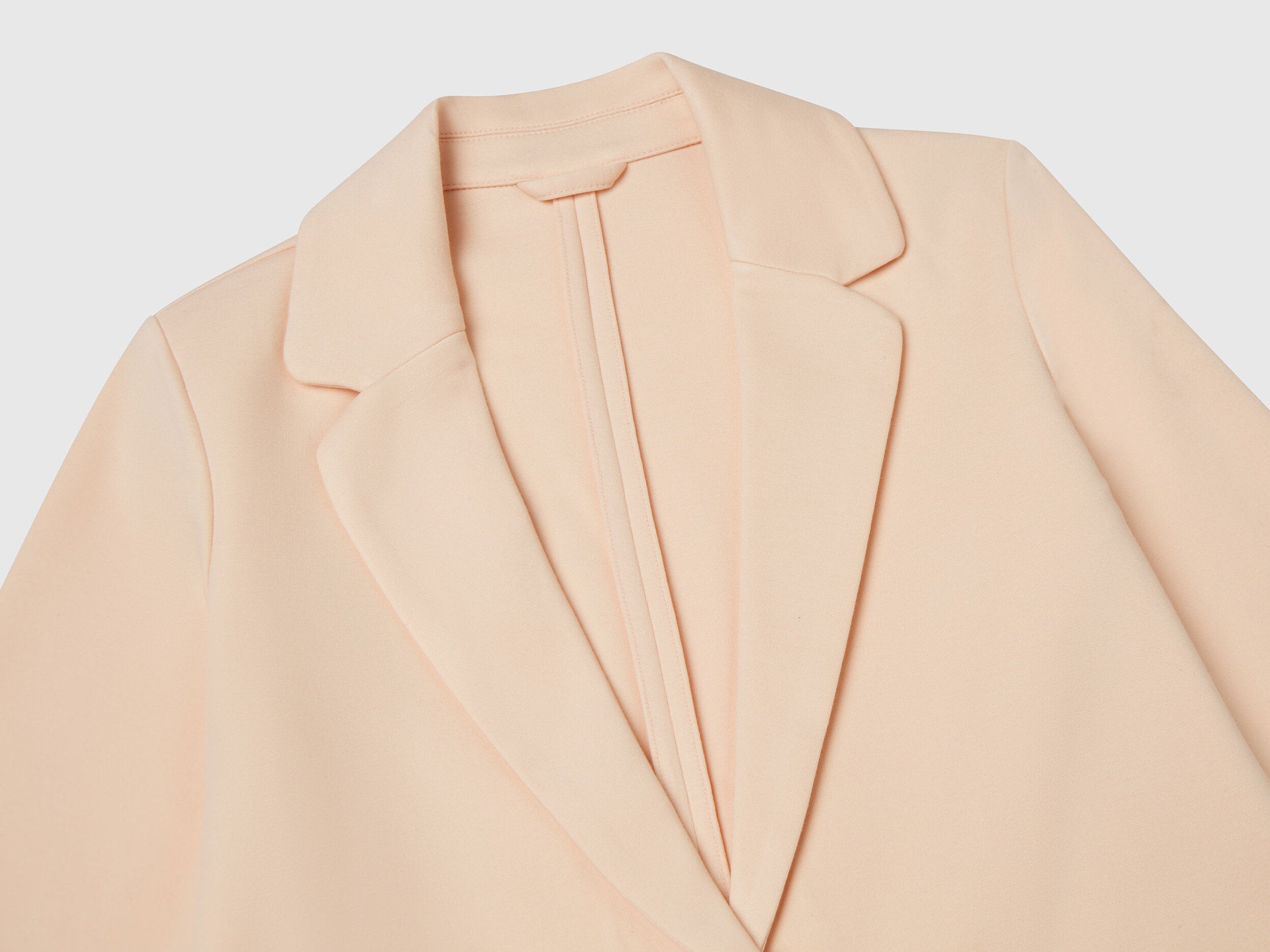 Close-up of the notched lapel and soft fabric of an elegant long blazer for women in a delicate peach shade, highlighting its refined details for the Kuwait fashion market.