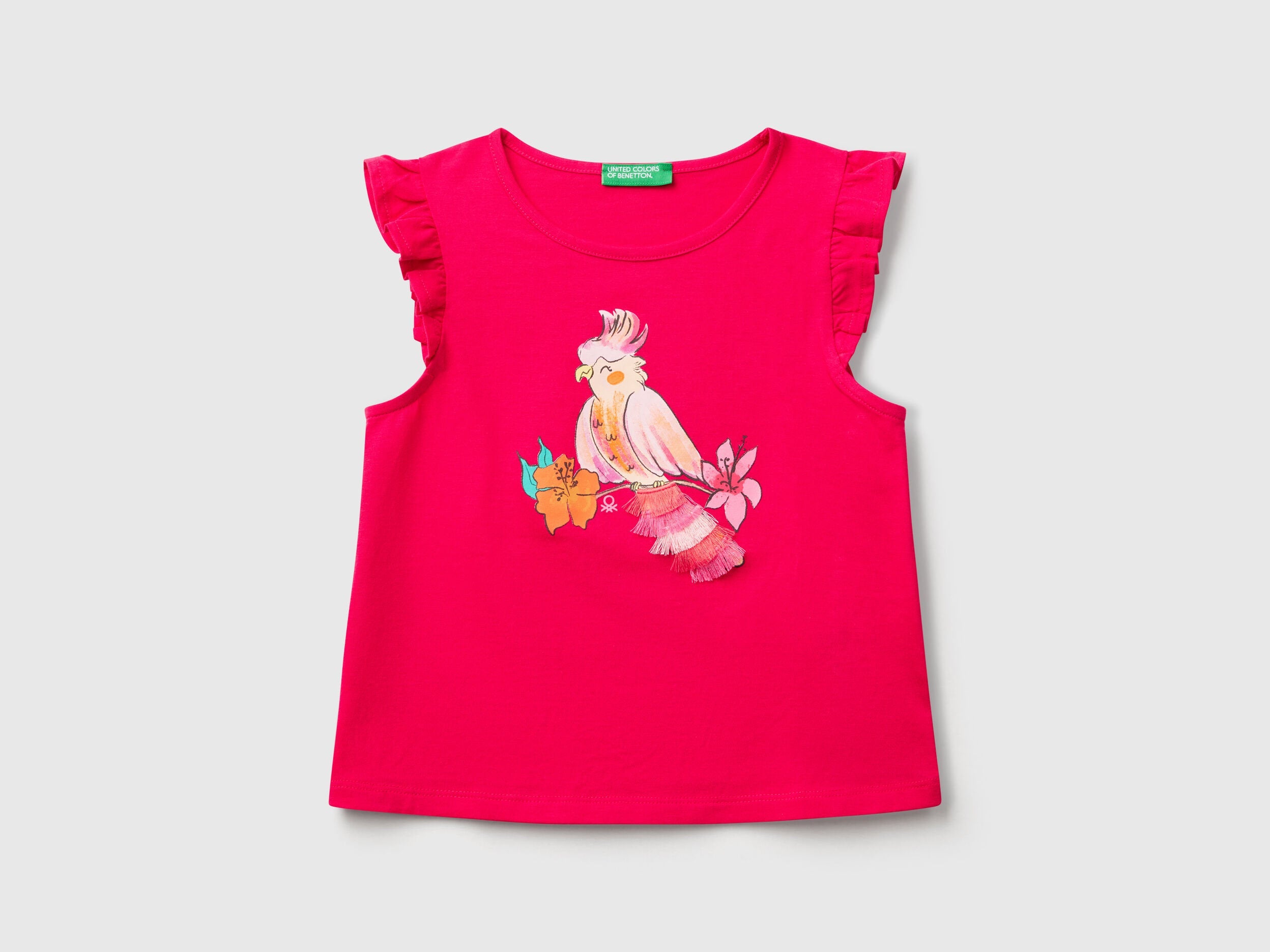 Front view of a fuchsia Benetton printed tank top with a colorful bird graphic and ruffle sleeves.