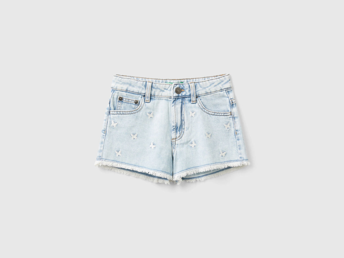 Front view of light wash denim shorts for girls with butterfly embroidery.