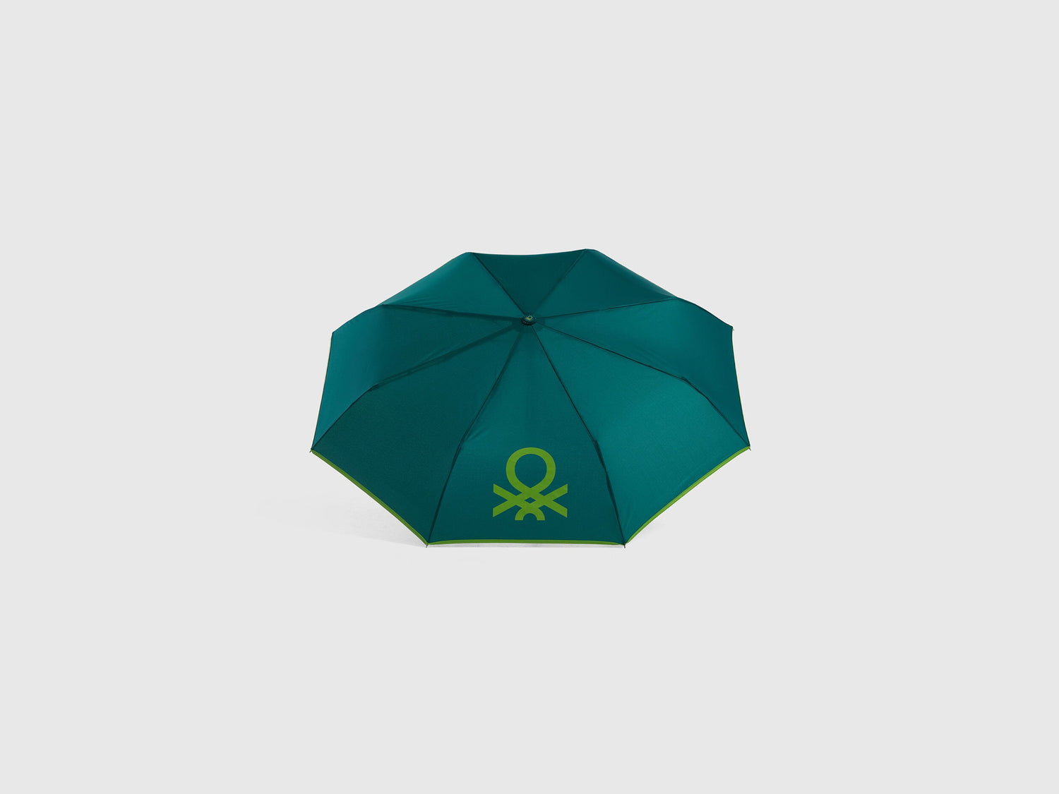 Open green Benetton umbrella, top view for rain protection.