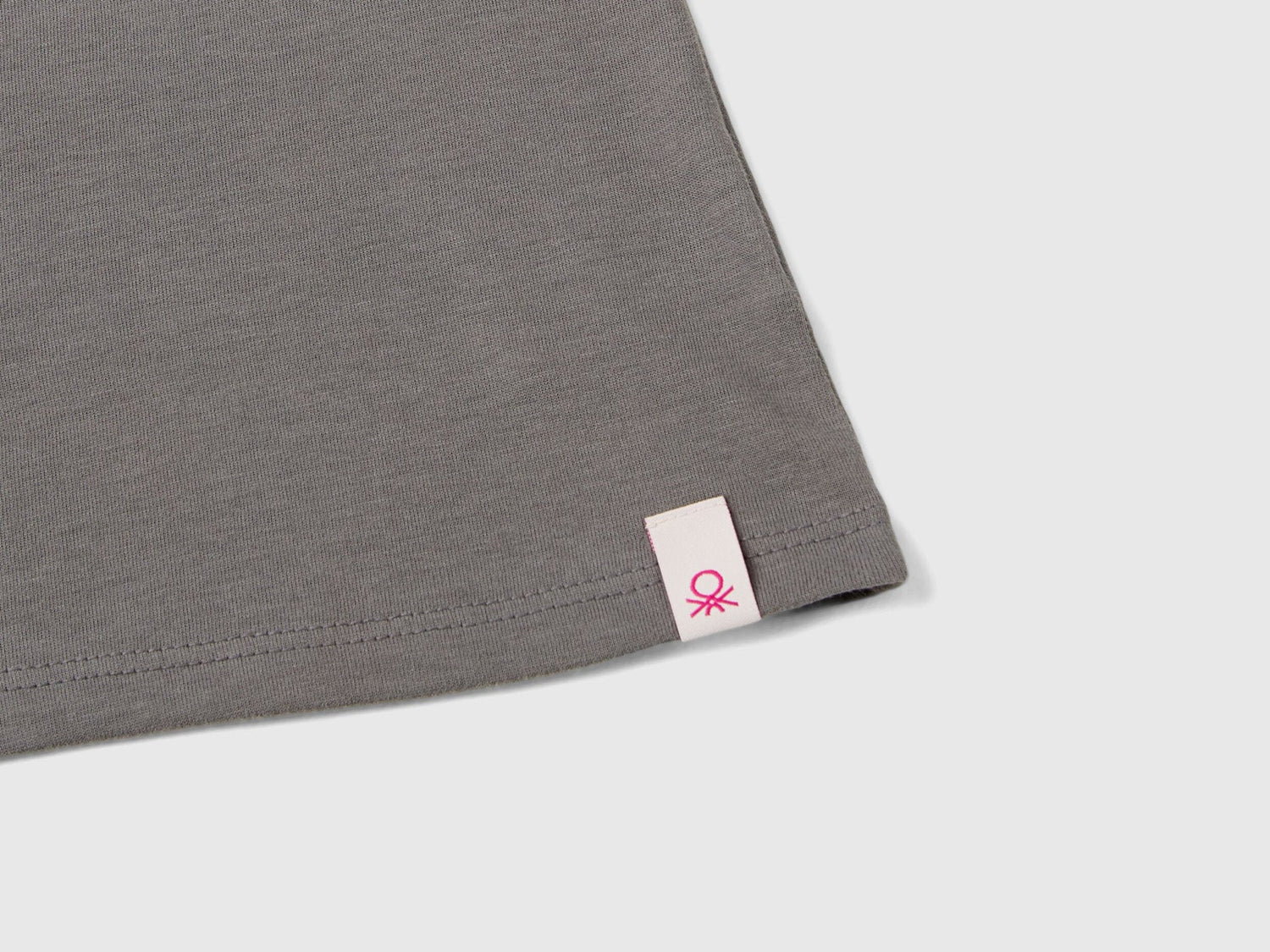 Close-up of the grey long-sleeve t-shirt hem, showing a small Benetton tag.