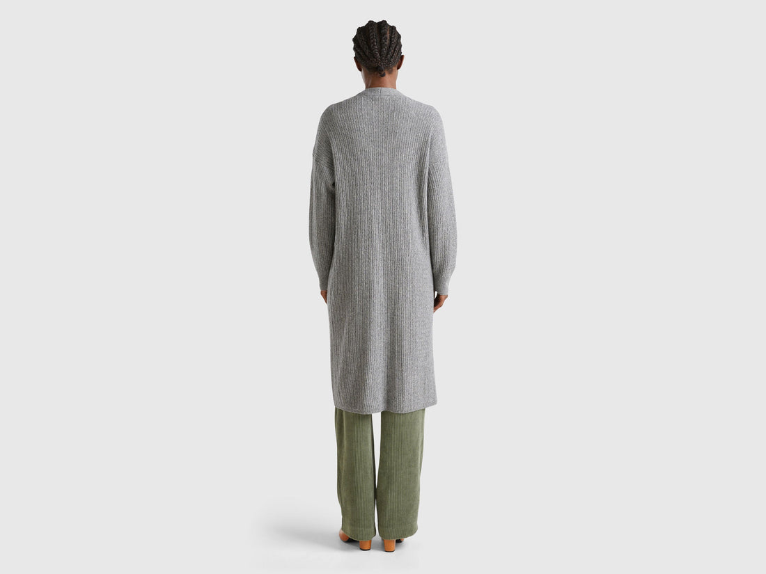 Back view: Woman in grey long cardigan (wool blend) over olive wide-leg pants. Textured knit.