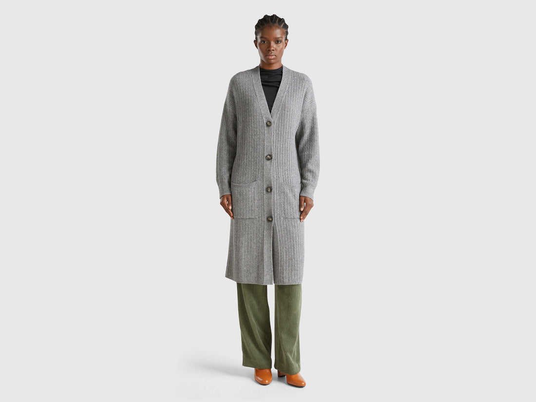 Front view: Woman in grey long cardigan (wool blend), buttoned, with olive wide-leg pants. Ribbed.
