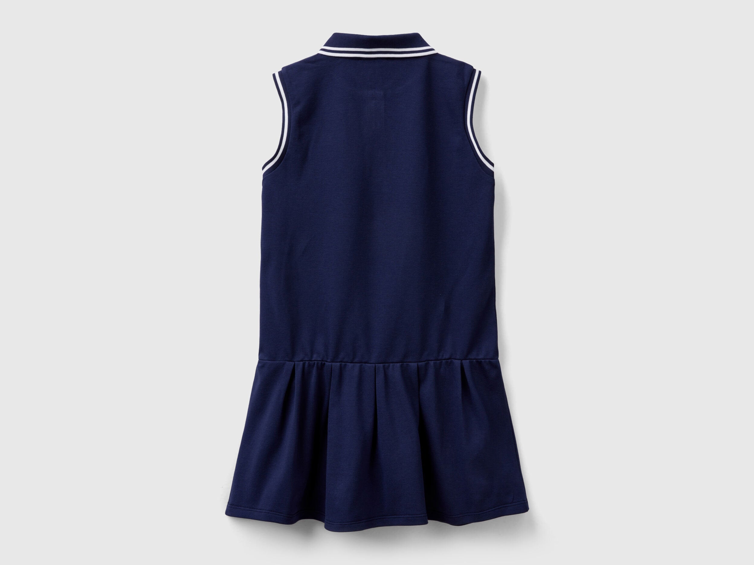 Back view of a navy blue polo dress for kids, with white striped trim on the collar and a ruffled skirt.