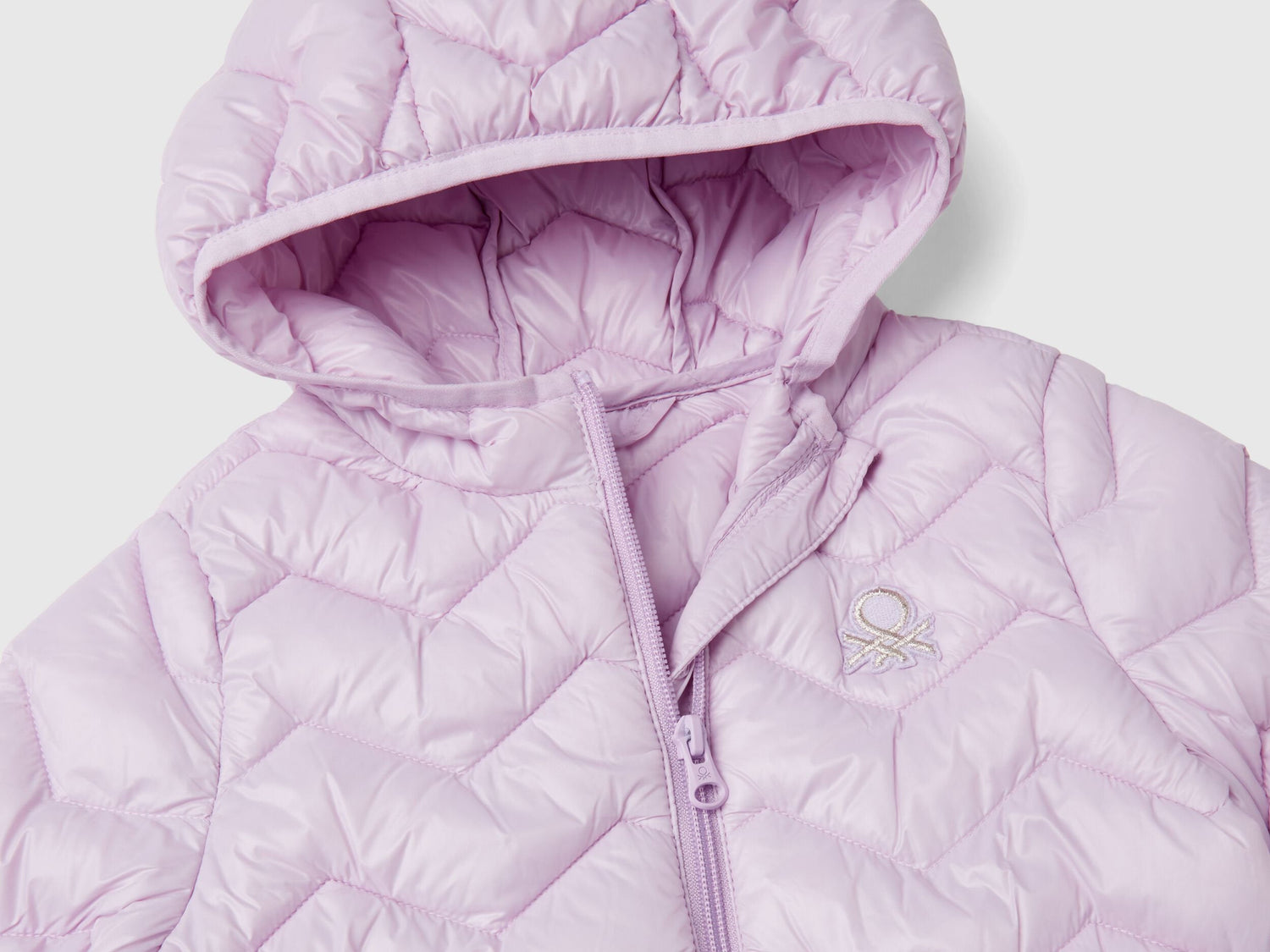 Close-up of a light pink padded jacket for a girl, showing hood, zipper, and logo.