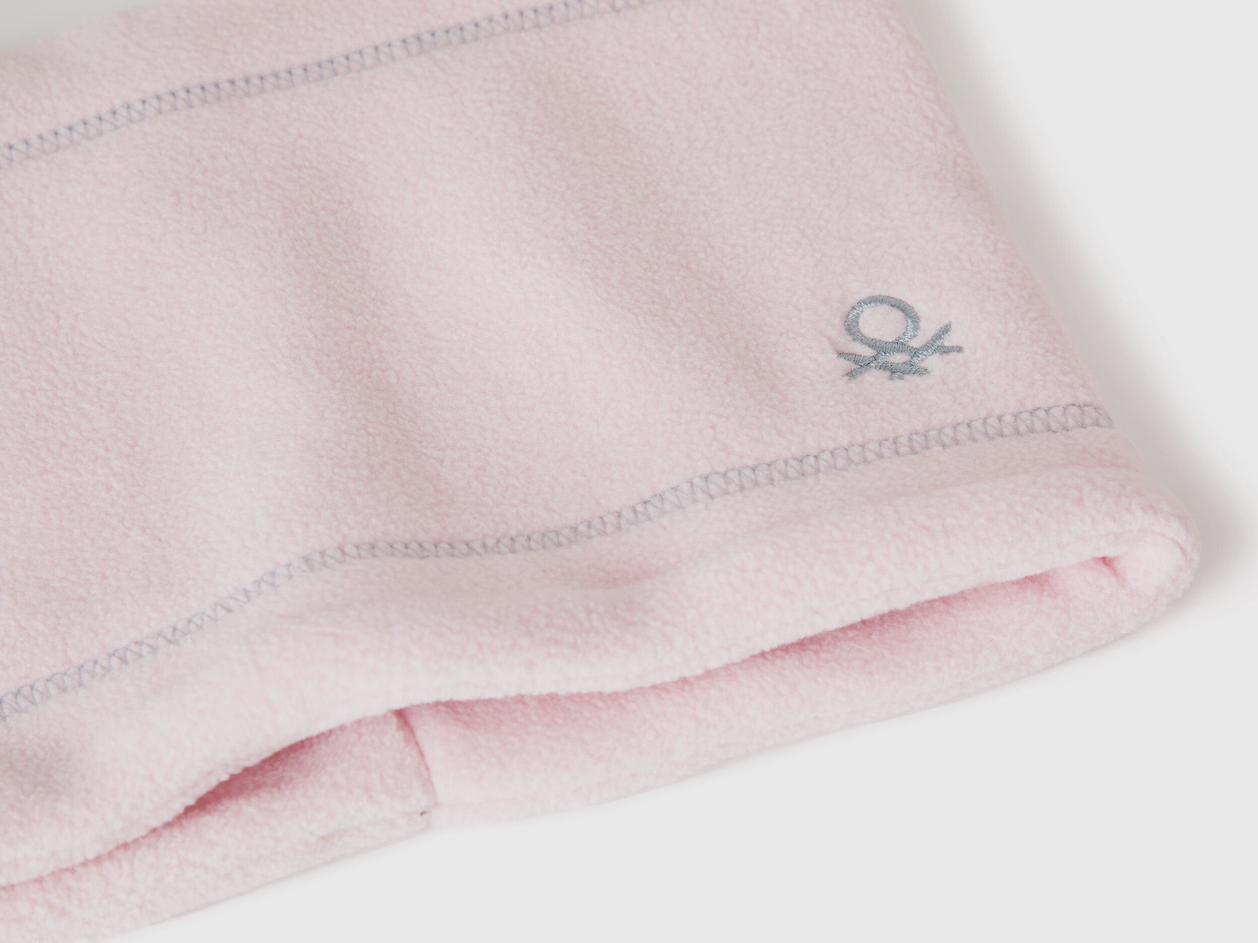 Close-up light pink fleece neck warmer with Benetton logo.