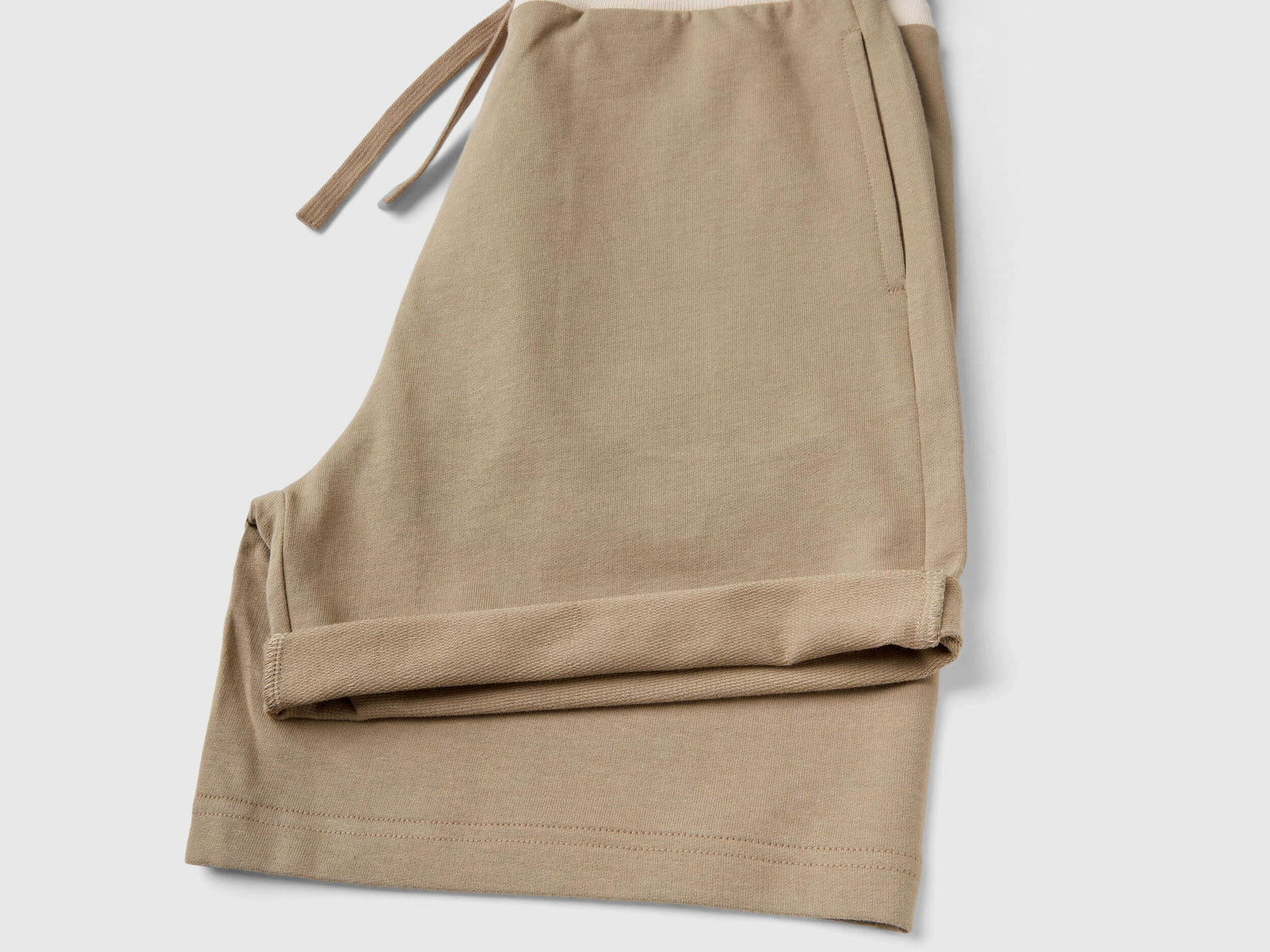 Folded lightweight beige sweat shorts showing the drawstring.