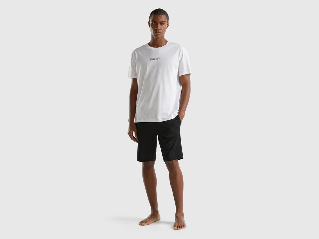 Full shot of a man wearing black cotton shorts and a white t-shirt.