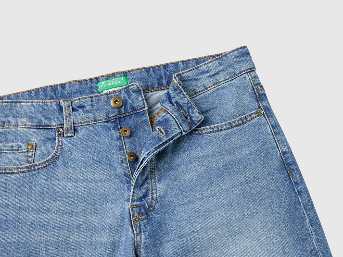 Close-up of the waistband and front button on blue five-pocket jeans.