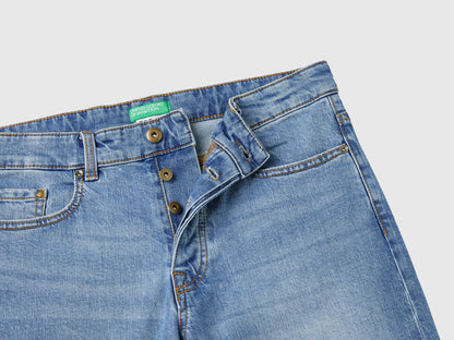 Close-up of the waistband and front button on blue five-pocket jeans.