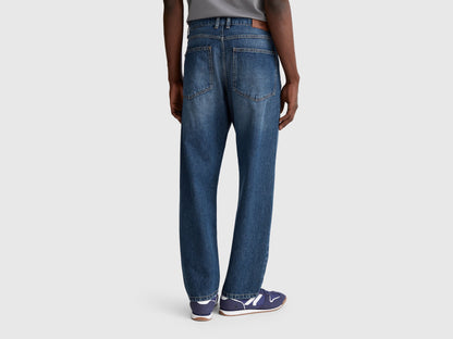 Full-length side view of a man wearing blue slim-fit jeans.