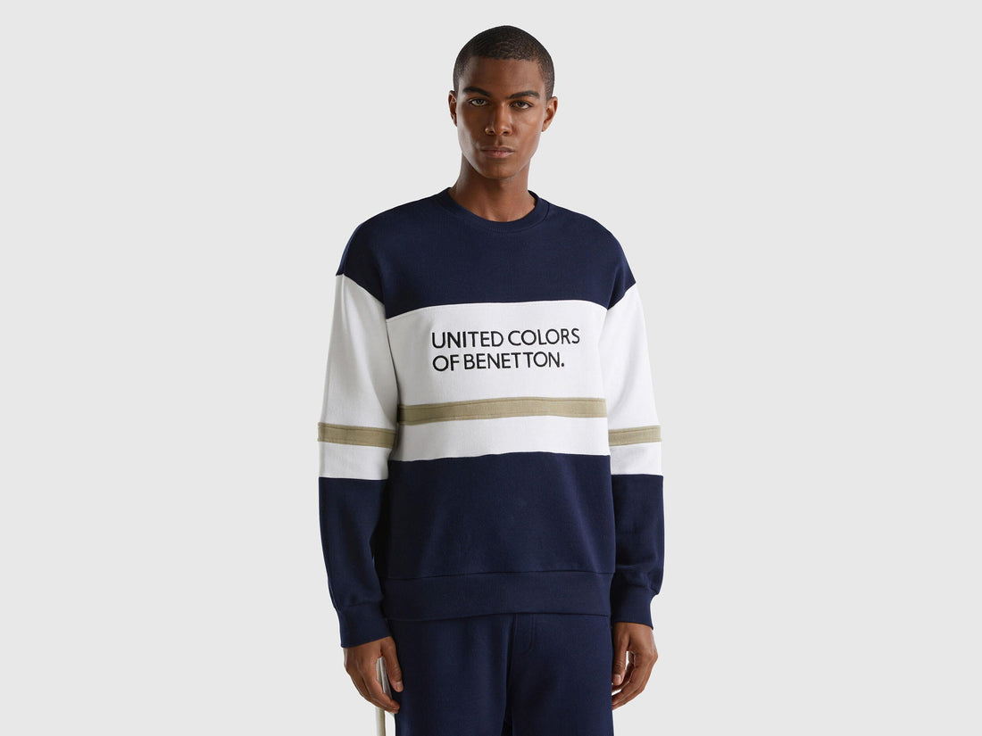Front view of a man wearing a dark blue sweatshirt with a black and white logo stripe across the chest.