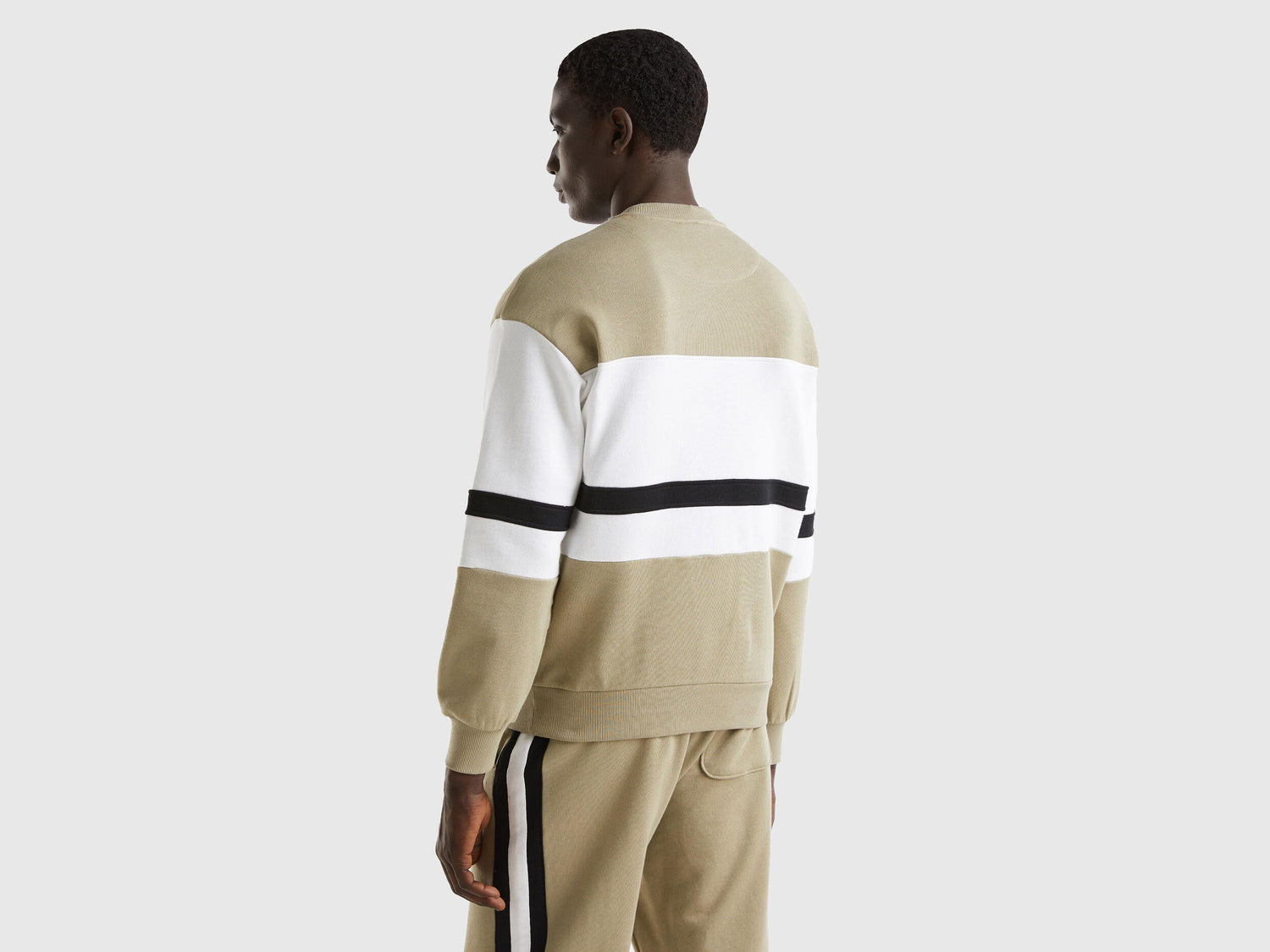 Back view of a man wearing a sage green sweatshirt with a black and white stripe.