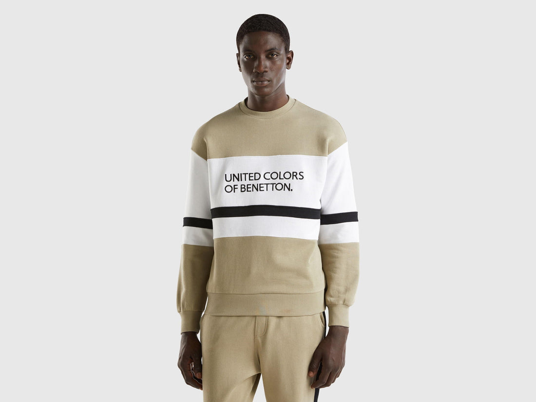 Front view of a man wearing a sage green sweatshirt with a black and white logo stripe across the chest.