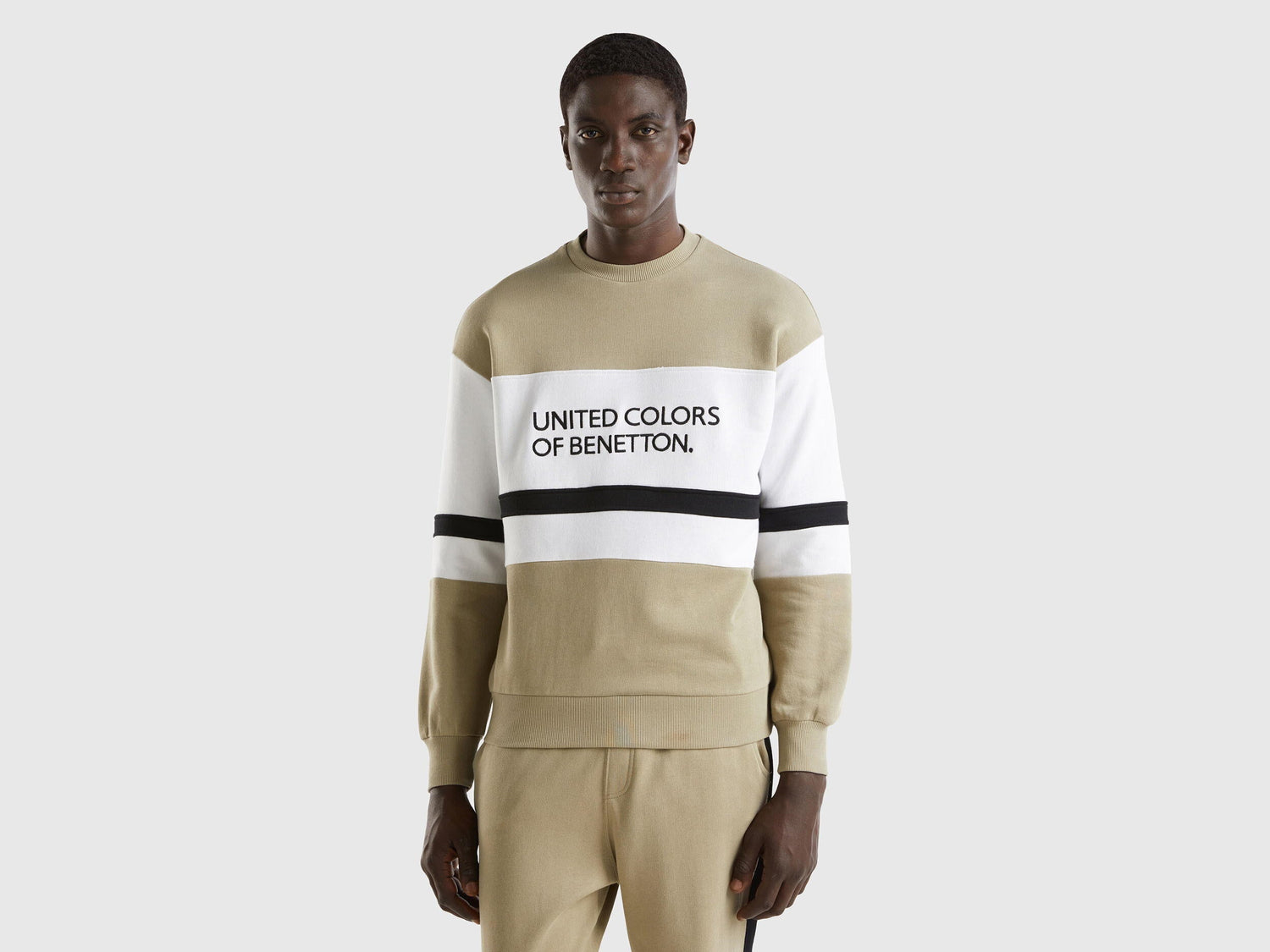 Front view of a man wearing a sage green sweatshirt with a black and white logo stripe across the chest.