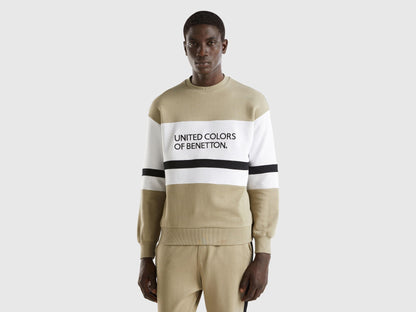 Front view of a man wearing a sage green sweatshirt with a black and white logo stripe across the chest.